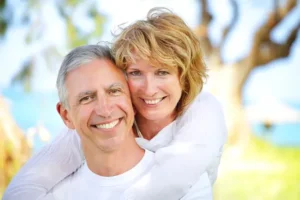 mature couple smiling outdoors near trees and water, Dental Veneers West Orange, NJ