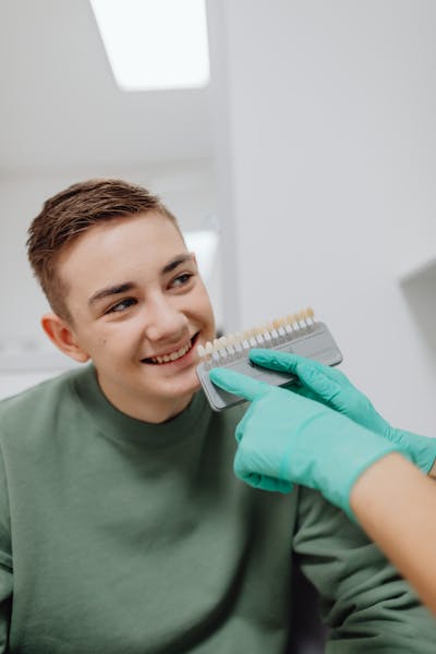 A Boy Smiling while a Person Wearing Latex Gloves is Holding a Dental Shade Guide